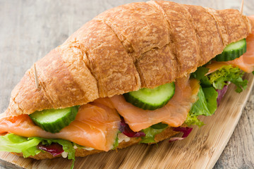 Croissant sandwich with salmon and vegetables on wooden table. 