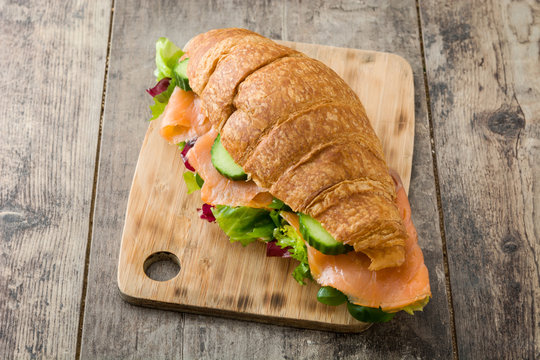 Croissant sandwich with salmon and vegetables on wooden table. 