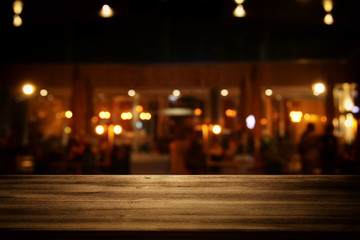 Image of wooden table in front of abstract blurred restaurant lights background.