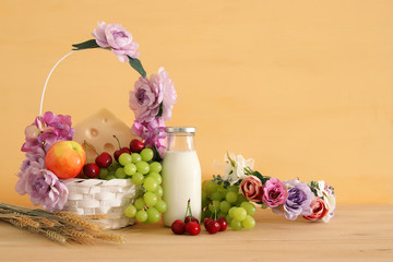 image of fruits and cheese in decorative basket with flowers over wooden table. Symbols of jewish holiday - Shavuot.