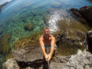 Partly blurred image because of drops of water. Young male explorer in adventure ready for snorkeling. Selfie shot at summer day at rock in the middle of the sea.