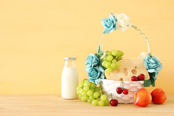 image of fruits and cheese in decorative basket with flowers over wooden table. Symbols of jewish holiday - Shavuot.