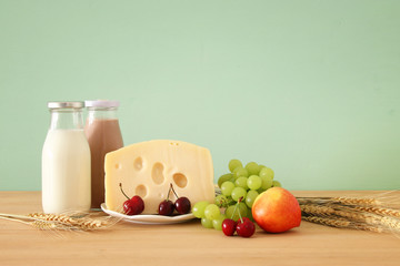 image of fruits and cheese in decorative basket with flowers over wooden table. Symbols of jewish holiday - Shavuot.
