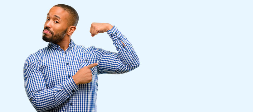 African american man with beard pointing biceps expressing strength and gym concept, healthy life its good isolated over blue background