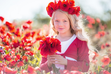 Pretty blonde child girl is wearing wreath from red flowers in poppy meadow