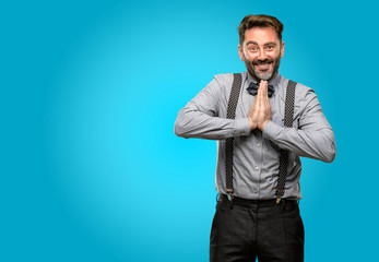 Middle age man, with beard and bow tie with hands together in praying gesture, expressing hope and please concept