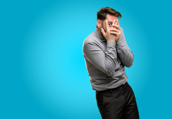 Middle age man, with beard and bow tie smiling having shy look peeking through fingers, covering face with hands looking confusedly broadly