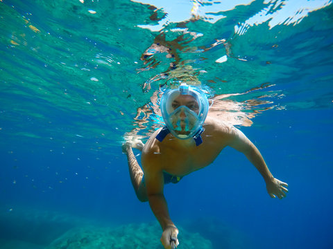 Underwater view of a young diver man swimming in the turquoise sea under the surface with snorkeling mask for summer vacation while taking a selfie with a stick.