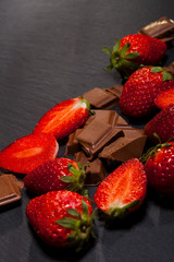 Fresh juicy strawberries with leaves and chocolate pieces on black background.