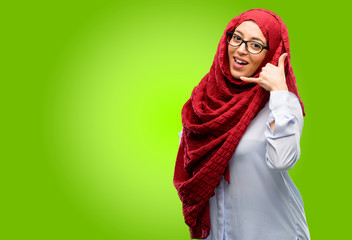 Young arab woman wearing hijab happy and excited making showing call me gesture with hand shaped like telephone
