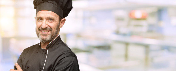 Senior cook man, wearing chef hat with crossed arms confident and happy with a big natural smile...