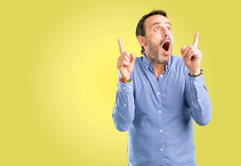 Handsome middle age man happy and surprised cheering expressing wow gesture pointing up