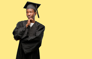Young african graduate student black man thinking and looking up expressing doubt and wonder