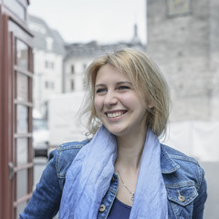 Beautiful blonde model appearance, stands next to a red phone booth.