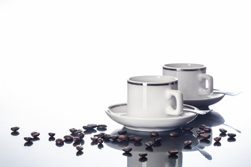 Espressotassen und Kaffeebohnen auf spiegelnder Tischplatte vor weißem Hintergrund
