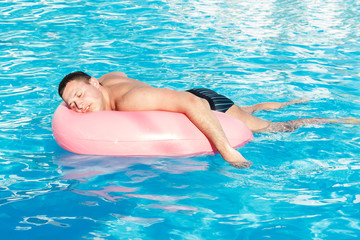 top view of young drunk guy swim with pink circle in pool. drunk guy on vacation in the hotel