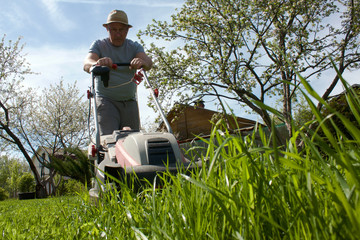 a middle-aged man mowing grass with a lawn mower