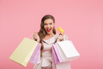 Photo of rich fashion woman 20s in dress smiling while holding different shopping bags and credit...