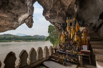 View of the Mekong River and many golden and wooden Buddha statues and religious offerings inside the Tham Ting Cave at the famous Pak Ou Caves near Luang Prabang in Laos. - obrazy, fototapety, plakaty