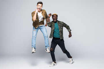 Portrait of a two mixed race cheerful young men jumping and celebrating isolated over white background
