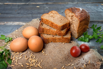 A cut loaf of bread on a wooden table among tomatoes, flour, parsley and chicken eggs. Advertising still life from baking.