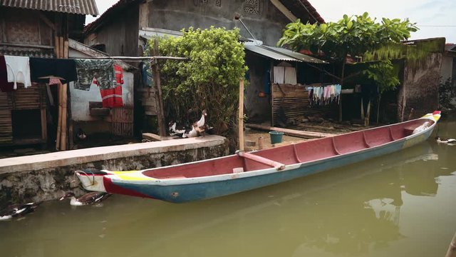 Village houses at river with ducks and small boat and drying clothes in Indonesia