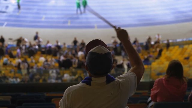 Middle-aged Sports Fan Seated At Stadium, Waving  His Team Flag, Watching Game. Football Fan Supporting His Team, 4K