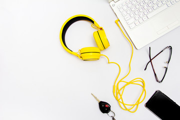Yellow headphones, notebooks, car keys, glasses and mobile. Placed on a white background.