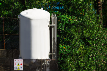 the metal cistern containing a water for supplying hotel visitors with comfortable conditions. the container standing outdoors under the sun near the plants and fence
