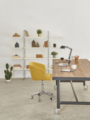 vertical office room style with wood table yellow office chair and devices with bookshelf.