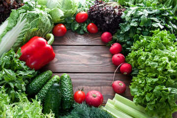 top view of green lettuce leaves, cucumber and red vegetables on wooden table with place for text centered