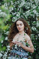 A beautiful girl in a dress stands next to a blooming cherry bush.