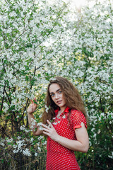 A beautiful girl in a dress stands next to a blooming cherry bush.