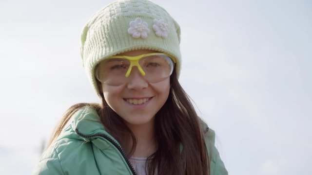 A girl waves a stick. a little girl in a green hat and glasses looks at the camera.