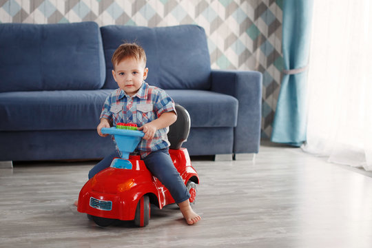 Boy child sits on a toy red car indoors