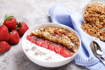 Acai banana strawberry smoothie bowl with chia seeds, fruits, berries, granola cereals, mixed nuts. Healthy vegan diet food. Raw ingredients breakfast on gray concrete background, copy space top view
