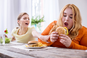 So tasty. Weak-willed overweight woman eating a sandwich and her friend stopping her