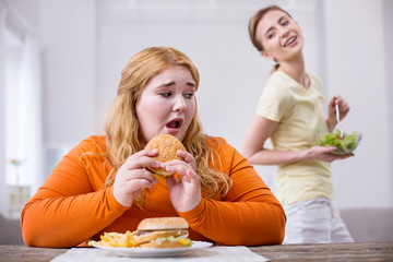 Mocking. Poor stout woman eating a sandwich and her slim friend smirking