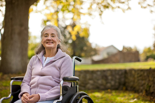 Portrait of a smiling senior woman sitting in a wheelchair inside a park.