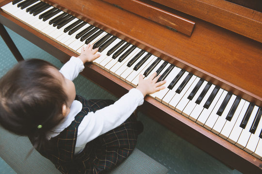 little well-dressed girl playing on wooden piano, top view