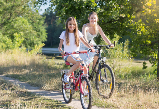 Happy smiling girl riding bicycle with young mother in field at hot summer day