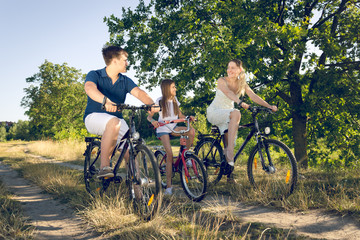 Toned image of happy smiling family having fun and riding on bicycles in field