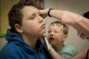 Young boy looking into his brother's ear as it is examined by a female doctor.