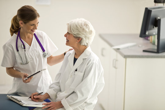 Smiling nurse and a female doctor having a discussion inside an exam room.