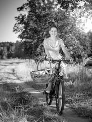 Black and white image of beautiful smiling woman riding on bicycle with big basket for picnic in park
