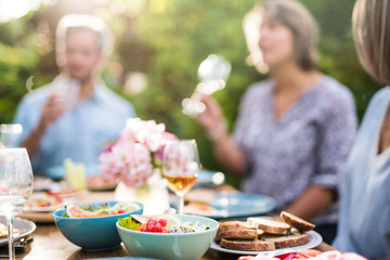 Focus on a colored salad in a bowl, Friends gather to share a meal around a table in the garden. Focus on the foreground
