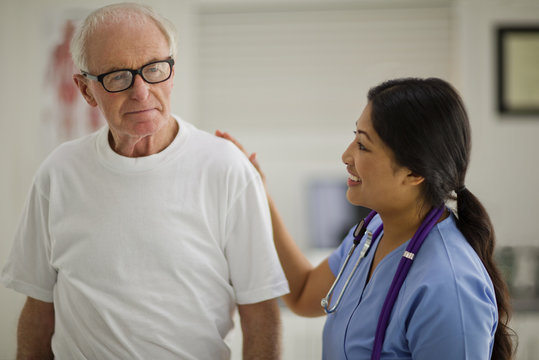 Smiling female nurse comforting an elderly male patient.