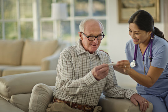 Smiling female nurse showing an elderly patient his result on a thermometer.