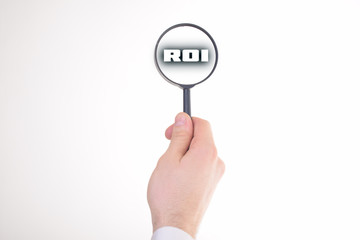 Businessman looking at a magnifying glass word:ROI