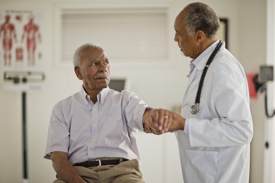 Senior man having his arm examined by a male doctor inside a doctor's office.